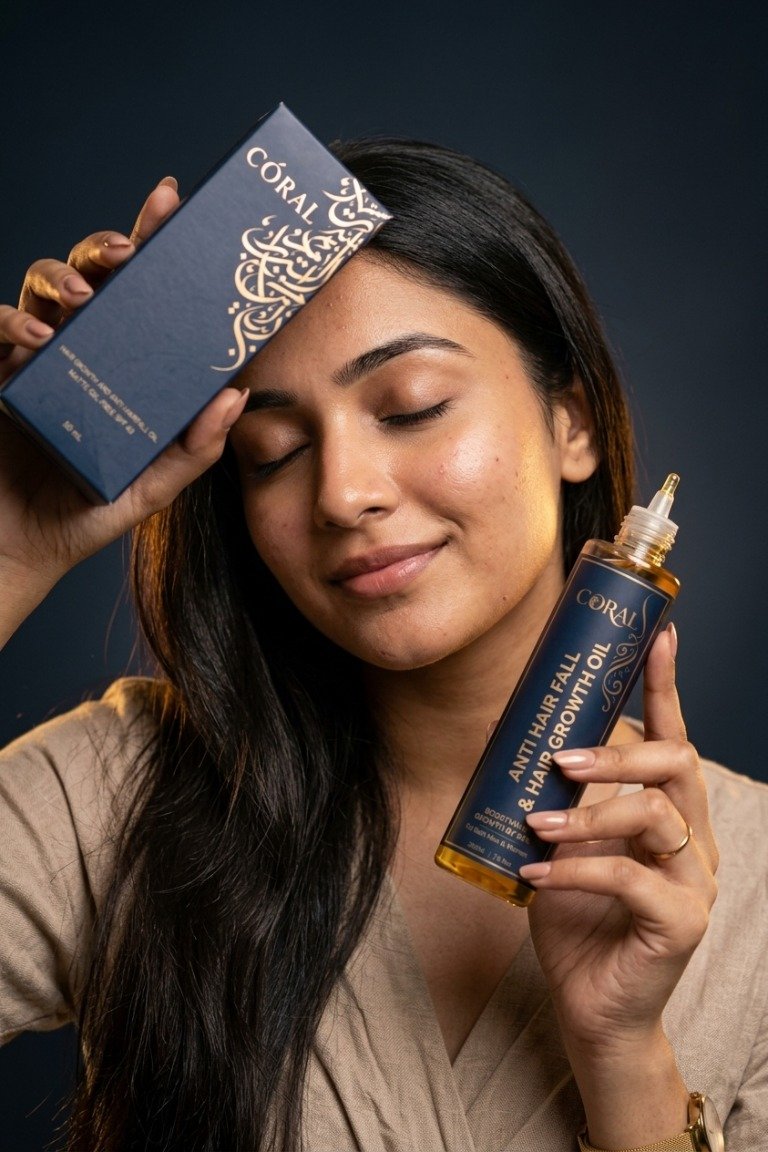 A woman holding CORAL hair oil and its matching product box.